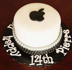 a white and black cake with an apple logo on the top is sitting on a wooden table