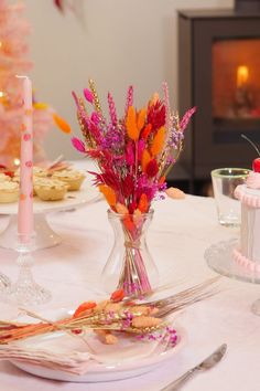 the table is set with pink and orange flowers in vases, cookies, and other desserts