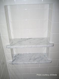 a marble shelf in the corner of a white tiled shower