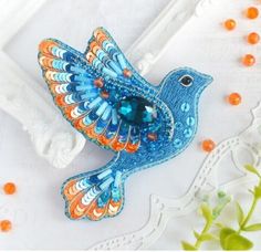 a blue and orange bird brooch sitting on top of a white doily next to flowers