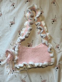 a crocheted purse sitting on top of a bed covered in pink and white fabric