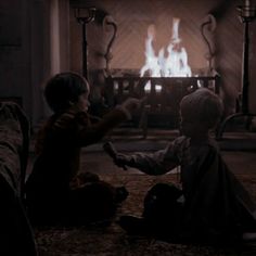 two children sitting on the floor in front of a fire place