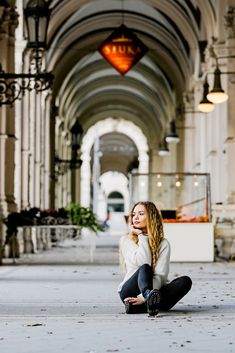 a woman is sitting on the ground in an old building with arches and lights above her