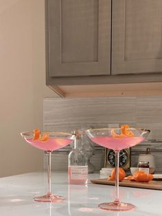 two martini glasses with orange peels in them sitting on a counter top next to a bottle