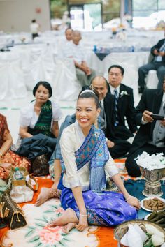 a woman sitting on the floor in front of other people at a wedding reception with food and drinks