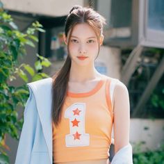 a woman with long hair wearing an orange shirt and blue blazer standing in front of trees