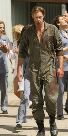 a man with blood all over his face walking in front of other people wearing scrubs