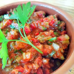 a brown bowl filled with lots of food on top of a wooden table next to a green leaf