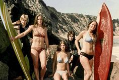 four women in bikinis are standing on the beach with their surfboards and posing for a photo