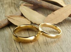 two gold wedding rings sitting on top of a wooden table next to leaves and twigs