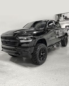 a black ram truck parked in a showroom next to other trucks and people looking at it