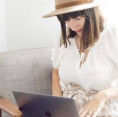 a woman sitting on a couch with a laptop computer in her lap and wearing a hat