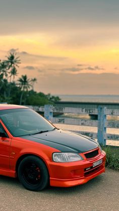 an orange and black car parked on the side of a road next to a body of water