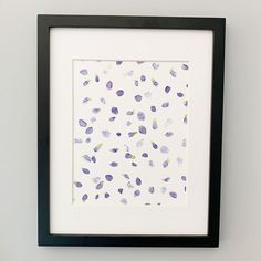 a white and black framed artwork with purple flowers on the bottom right corner, in front of a gray wall