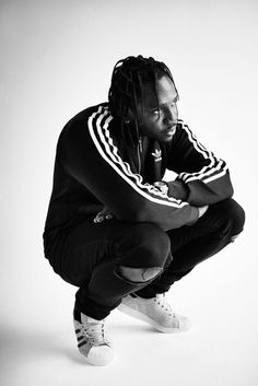 a man with dreadlocks squatting down in front of a white background wearing adidas