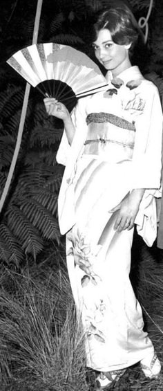 an old photo of a woman in kimonos holding a fan and posing for the camera