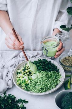 a person is preparing food on a plate with greens and dressing in mason jars next to them