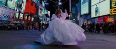 a woman in a white dress is walking down the street at night with her arms up