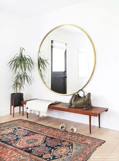 a round mirror sitting on top of a wooden table next to a rug and potted plant