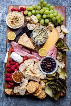 a wooden platter filled with cheese, crackers and fruit