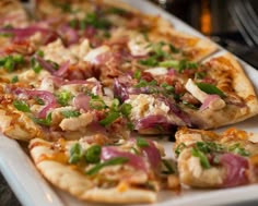 a pizza with onions, cheese and other toppings on a white plate sitting on a table