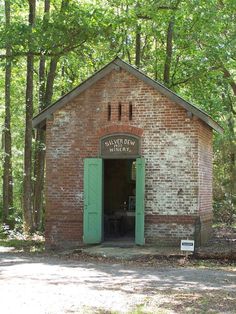 an old brick building in the woods with green doors and shutters on each side