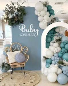 a baby shower with balloons and greenery on the wall, next to a wicker chair