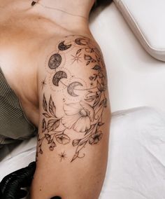 a woman's arm with flowers and moon tattoos on her left arm, sitting on a bed