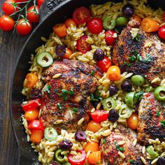 a skillet filled with pasta and meat covered in olives, tomatoes, peppers, and green beans