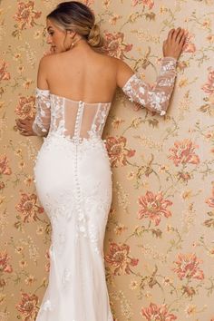 a woman in a wedding dress leaning against a wall with her back to the camera