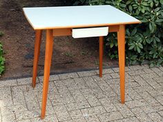 an orange table with a white drawer on it sitting in front of some bushes and shrubbery