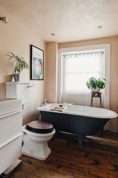 a bathroom with a tub, toilet and plant on the window sill in it