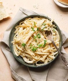 a bowl filled with pasta and parsley on top of a table next to bread