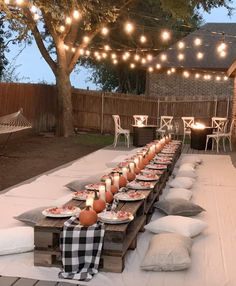 a long table is set with plates and candles on it for an outdoor dinner party