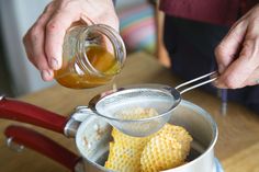 a person pouring honey into a pot filled with corn on the cob