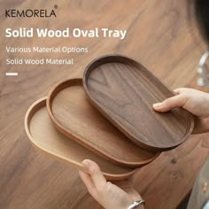 two wooden oval trays are stacked on top of each other, with one being held by a woman's hand