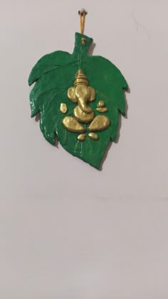 a green and gold leaf shaped ornament hanging on a wall with an elephant