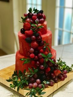 a three tiered cake with berries and greenery on the top is sitting on a cutting board