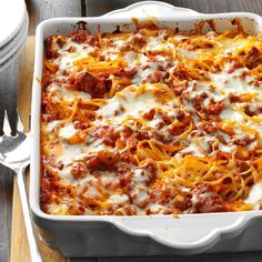 a casserole dish with meat and cheese in it on a wooden table next to silverware