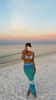 a woman standing on top of a sandy beach next to the ocean wearing a mask