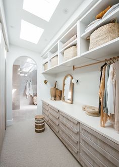 a walk in closet filled with lots of clothes and baskets on top of wooden shelves