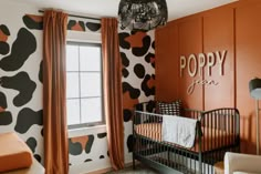 a baby's room decorated in black, orange and white with cow print on the walls