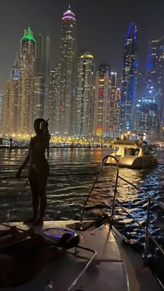 a woman standing on the edge of a boat in front of a city at night