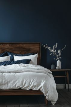 a bed with white and blue sheets in a dark colored room next to a wooden table