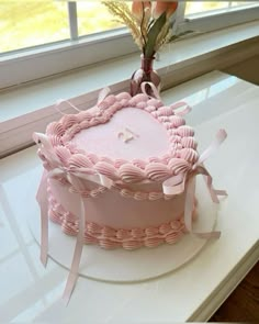 a pink heart shaped cake sitting on top of a white table next to a window