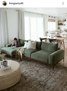 a woman sitting on top of a green couch in a living room next to a window