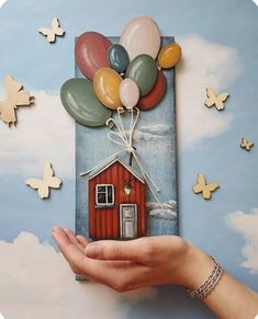 a person holding up a card with balloons and a house in the sky on it