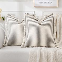 two striped pillows on a white couch in front of a wall with a framed photograph