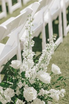 white flowers and greenery sit in front of the rows of white chairs at an outdoor ceremony