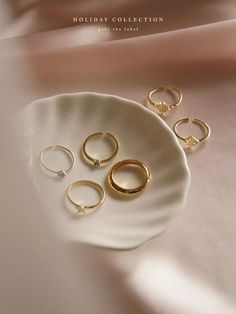 five gold rings sitting on top of a white plate next to another set of jewelry